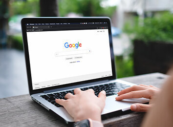 Hände auf Laptop-Tastatur mit geöffneter Google-Suchmaschine auf dem Bildschirm