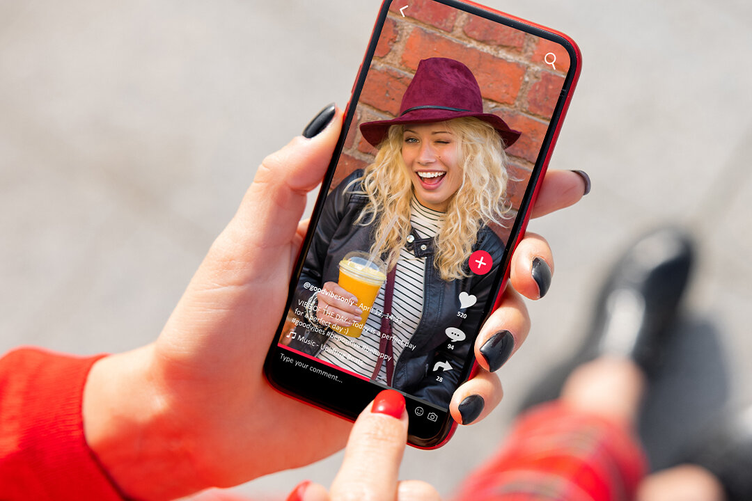 Weibliche Hände halten ein Smartphone mit TikTok.