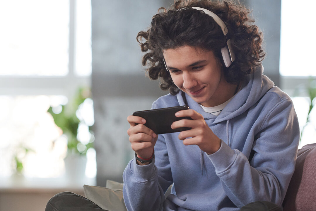 Junge mit Kopfhörern spielt im SChneidersitz auf seinem Smartphone