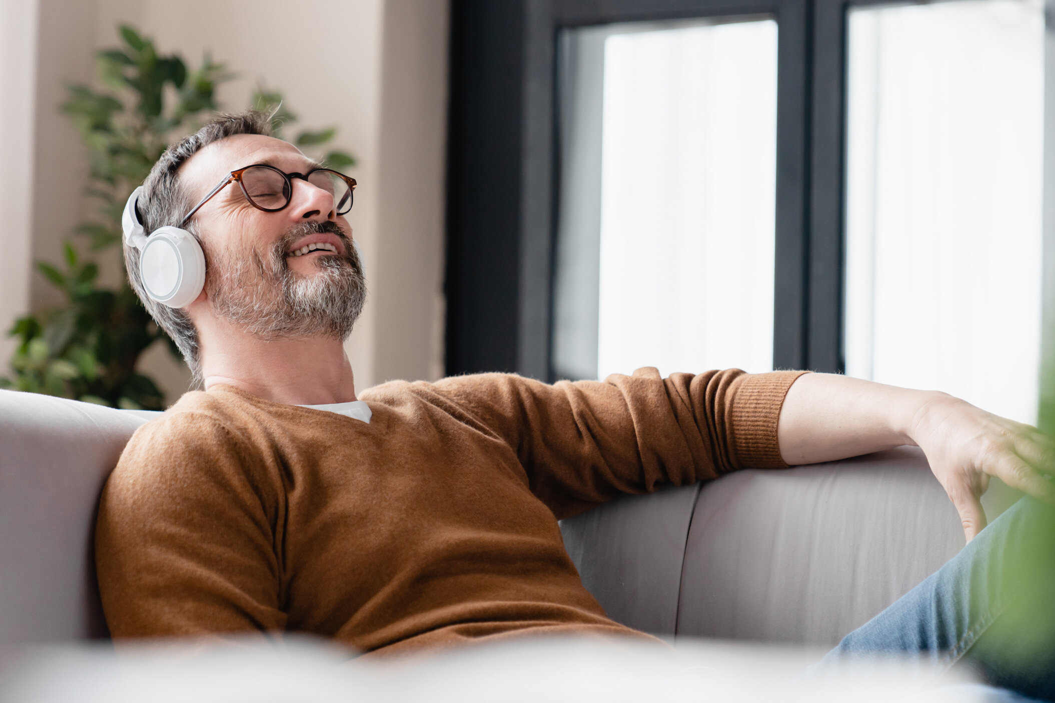 Entspannter Mann mit Kopfhörern auf Sofa, 7Mind App Integration, Wellness-Moment