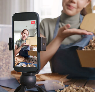 Mädchen präsentiert vor der Smartphone-Kamera einen offenen Karton mit umweltfreundlicher Verpackung.