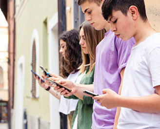 Zum Beitrag: Social Media & Mental Health Zu sehen: Vier Jugendliche lehnen mit Smartphones an Hauswand
