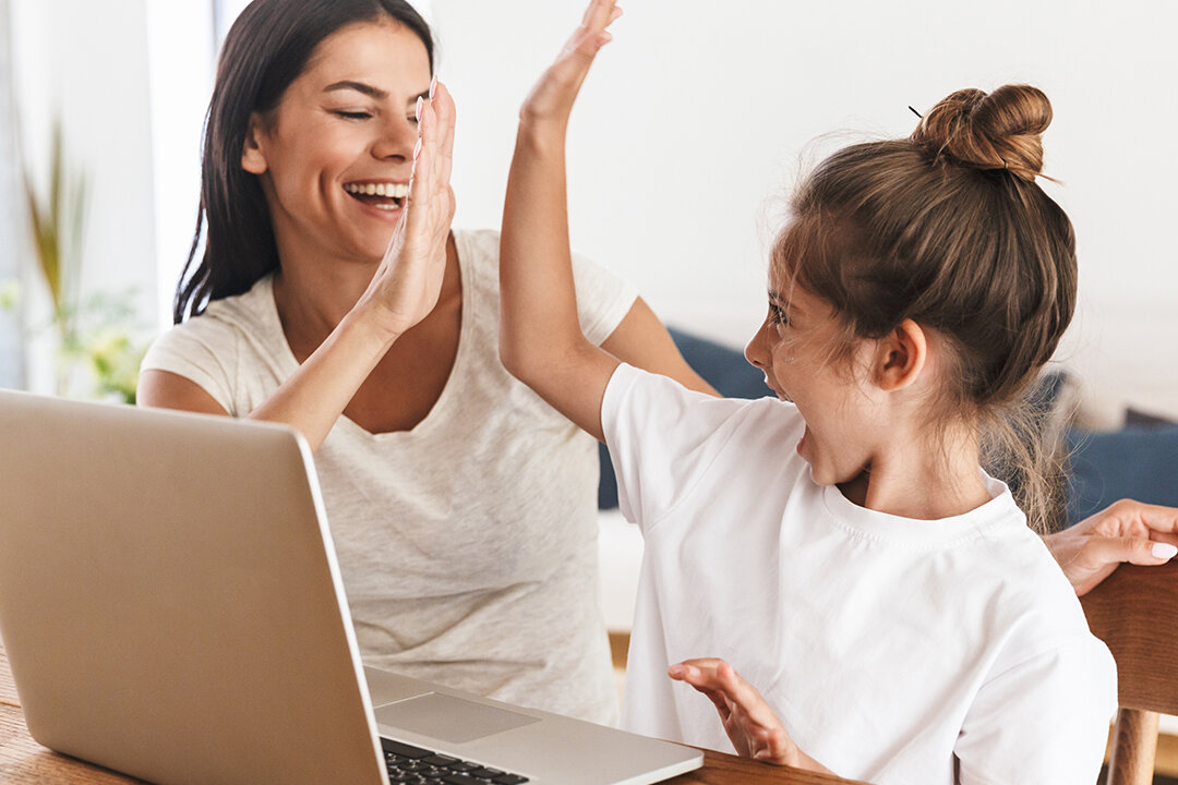  Eine Frau und ein Mädchen sitzen lachend an einem Laptop und geben sich ein High Fove