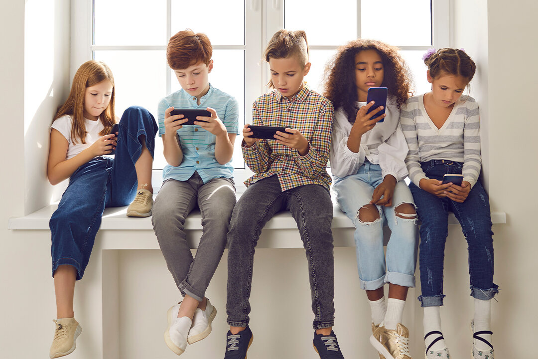 Fünf Kinder sitzen nebeneinander auf einer Fensterbank und schauen konzentriert auf ihre Smartphones.