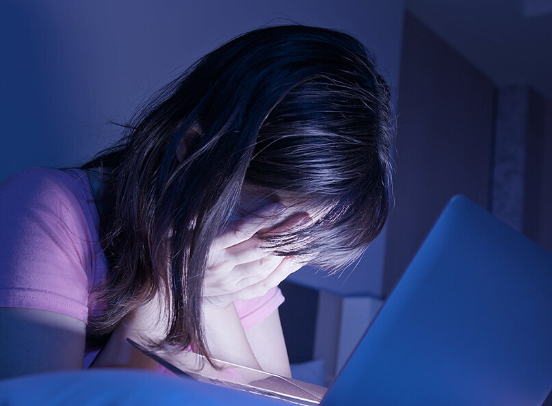 Jugendliche sitzt nachts vor einem Laptop und hält verzweifelt den Kopf in den Händen.