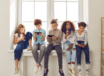 Fünf Kinder sitzen nebeneinander auf einer Fensterbank und schauen konzentriert auf ihre Smartphones.