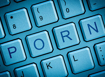 PORN-Schriftzug auf einer Computer-Tastatur in blauem Licht dargestellt.