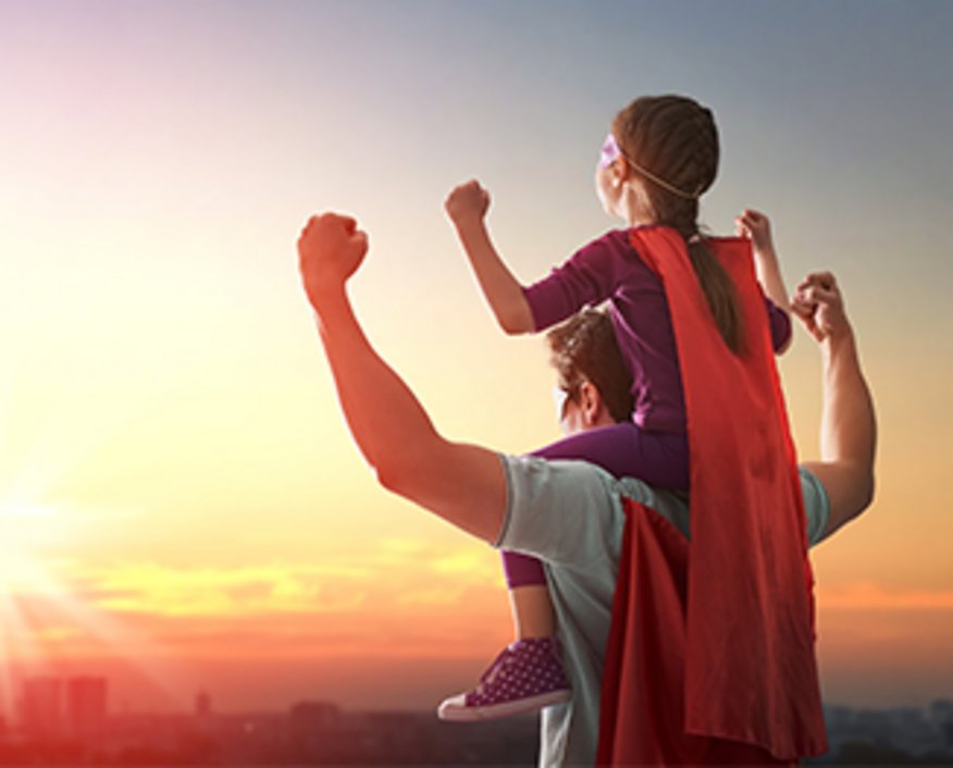 Mann mit Superheldencape trägt Mädchen mit Superheldencape auf den Schultern