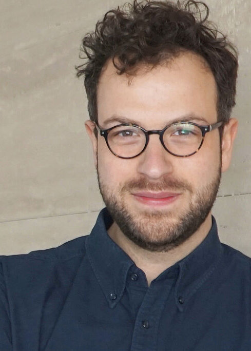 Porträt von Maximilian Schober mit Brille vor einem hellen, neutralen Hintergrund.