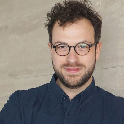 Porträt von Maximilian Schober mit Brille vor einem hellen, neutralen Hintergrund.