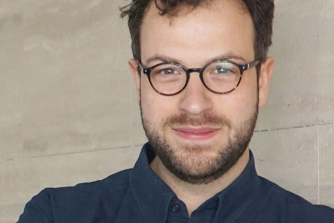 Porträt von Maximilian Schober mit Brille vor einem hellen, neutralen Hintergrund.