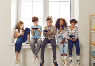 Fünf Kinder sitzen nebeneinander auf einer Fensterbank und schauen konzentriert auf ihre Smartphones.