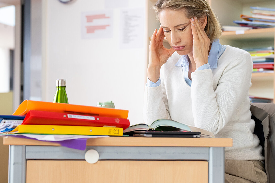 Lehrerin an Pult reibt sich die Schläfen