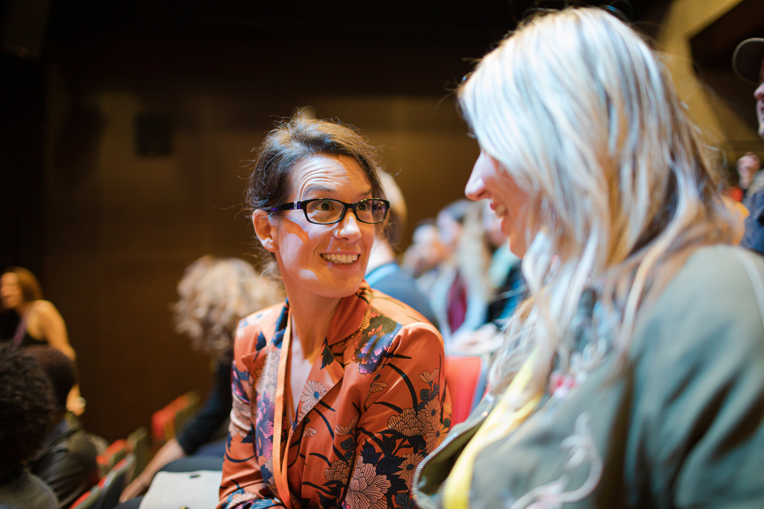 Zwei Geschäftsfrauen unterhalten sich während einer Konferenz im Publikum.