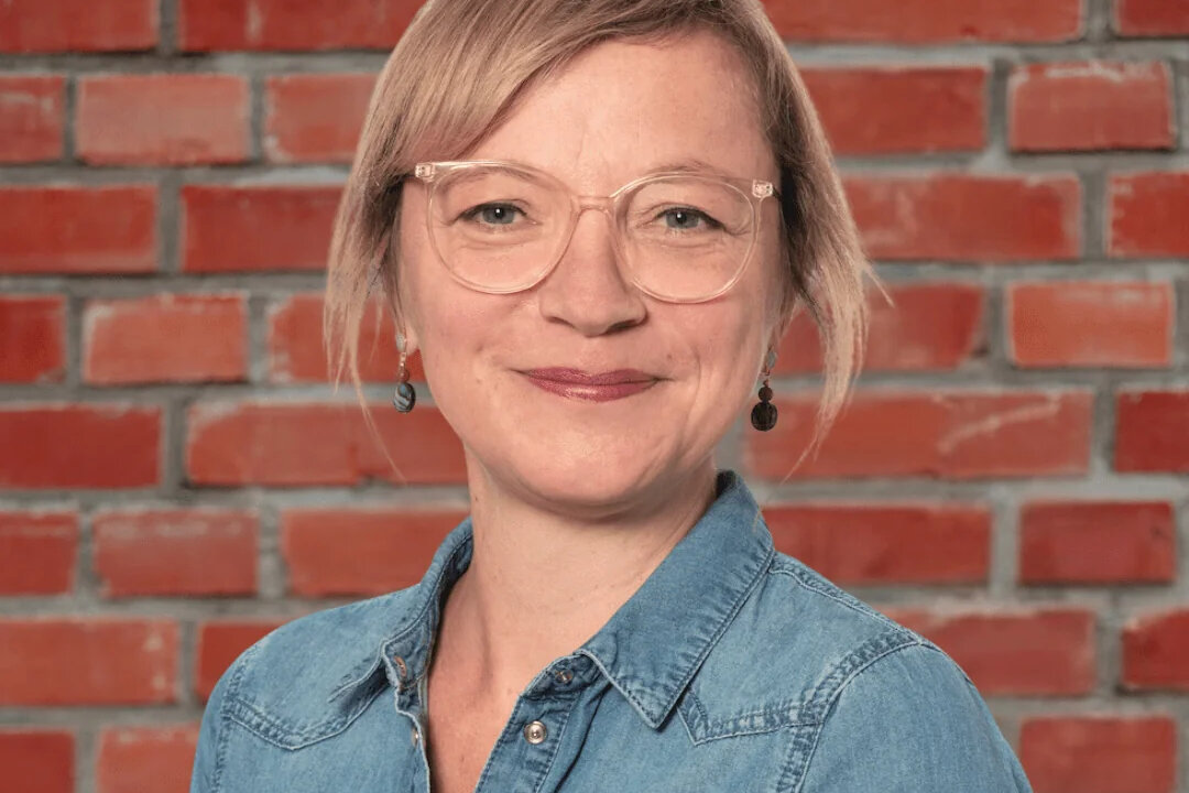 Porträt von Meike Wiggers, Gastautorin bei BARMER Durchblickt, mit blonden Haaren und Brille vor roter Backsteinwand.