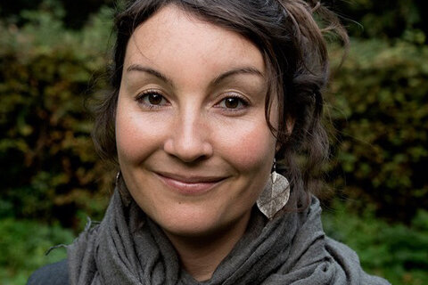 Anne Hackenberger, Redakteurin, Porträt mit warmem Lächeln, dunkle lockige Haare, grüner Hintergrund