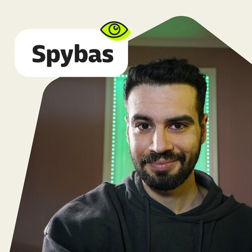 Porträt von Spyridon (Spybas), dunkler Hoodie, grüne LED-Lichter, Label „Spybas“.