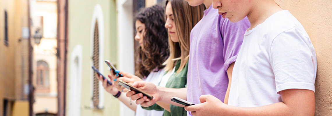 Zum Beitrag: Social Media & Mental Health Zu sehen: Vier Jugendliche lehnen mit Smartphones an Hauswand