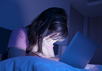 Jugendliche sitzt nachts vor einem Laptop und hält verzweifelt den Kopf in den Händen.