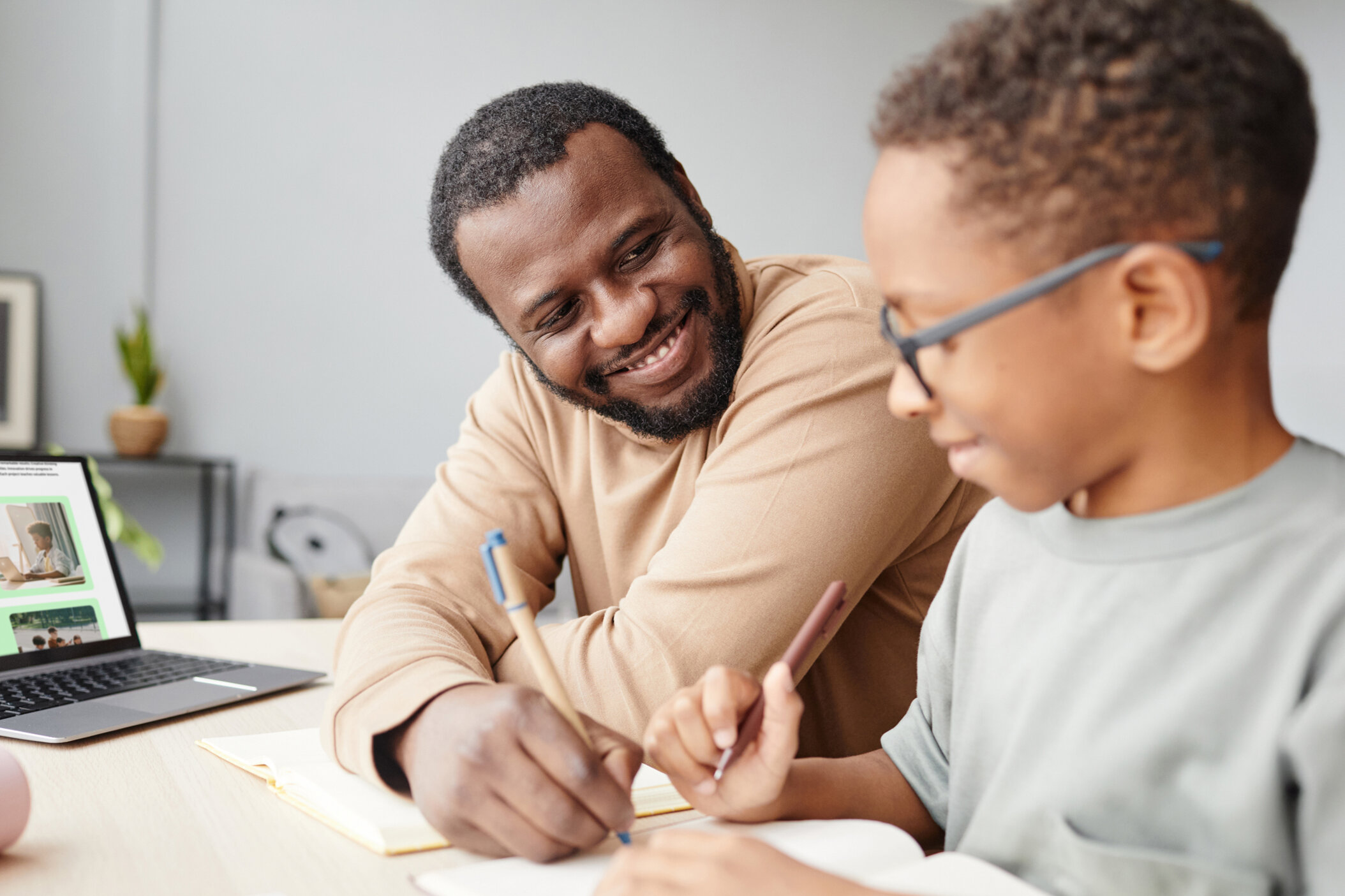 Vater und Kind mit Brille arbeiten gemeinsam am Laptop und mit Dokumenten – digitale Lernbegleitung, Eltern-Mentoring, Gesundheitskompetenz