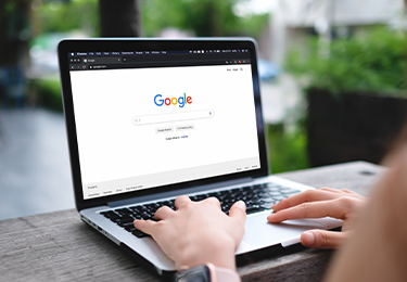 Hände auf Laptop-Tastatur mit geöffneter Google-Suchmaschine auf dem Bildschirm