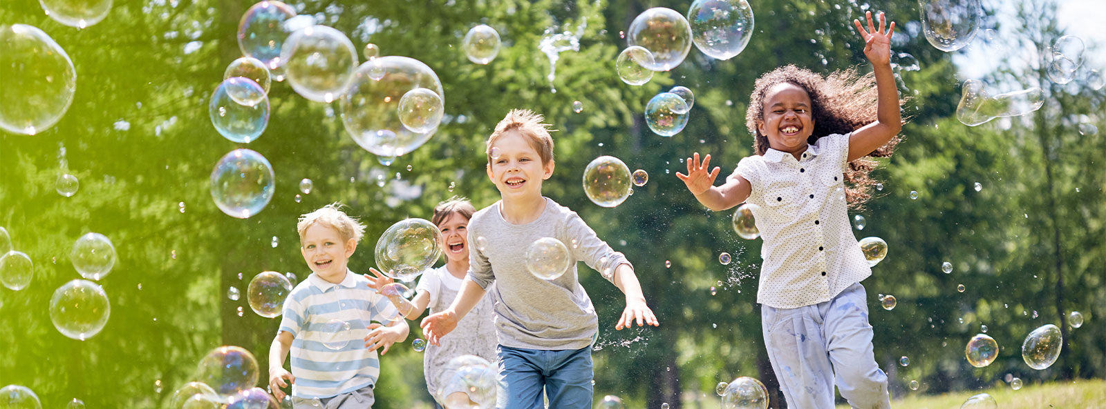 Vier Kinder rennen lachend über eine Wiese und spielen mit Seifenblasen.