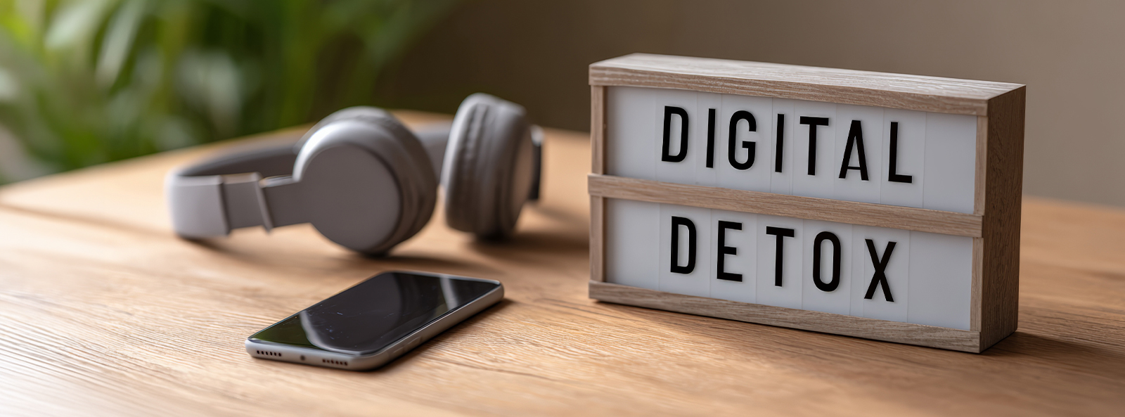 Leuchtbox mit Aufschrift „Digital Detox" auf Holzoberfläche, daneben abgelegtes Smartphone und Kopfhörer – Symbol für digitale Auszeit im Familienalltag