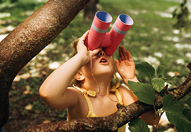 Kleines Mädchen schaut im Wald durch eine selbst gebastelte Papprohr-Fernglas in die Ferne