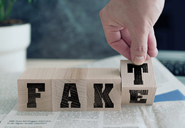 Vier Holzwürfel mit Buchstaben bilden ein Wort. Eine Hand bewegt den letzten Würfel, so dass man "Fake" oder "Fakt" lesen kann.