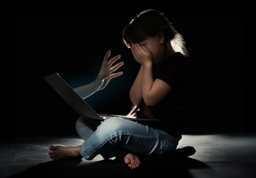 Kind vor Laptop, verdeckt das Gesicht, symbolisch für Online-Gefahren.