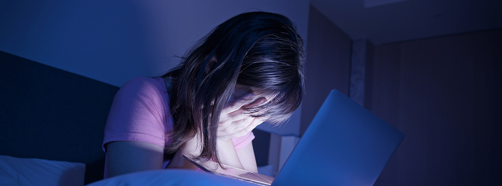 Jugendliche sitzt nachts vor einem Laptop und hält verzweifelt den Kopf in den Händen.