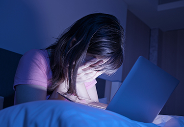 Jugendliche sitzt nachts vor einem Laptop und hält verzweifelt den Kopf in den Händen.