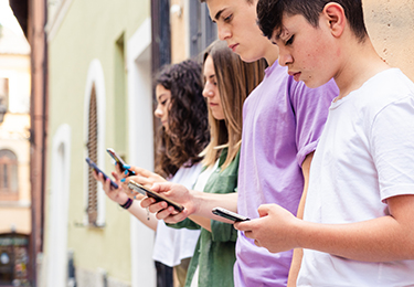 Vier Jugendliche lehnen mit Smartphones an Hauswand