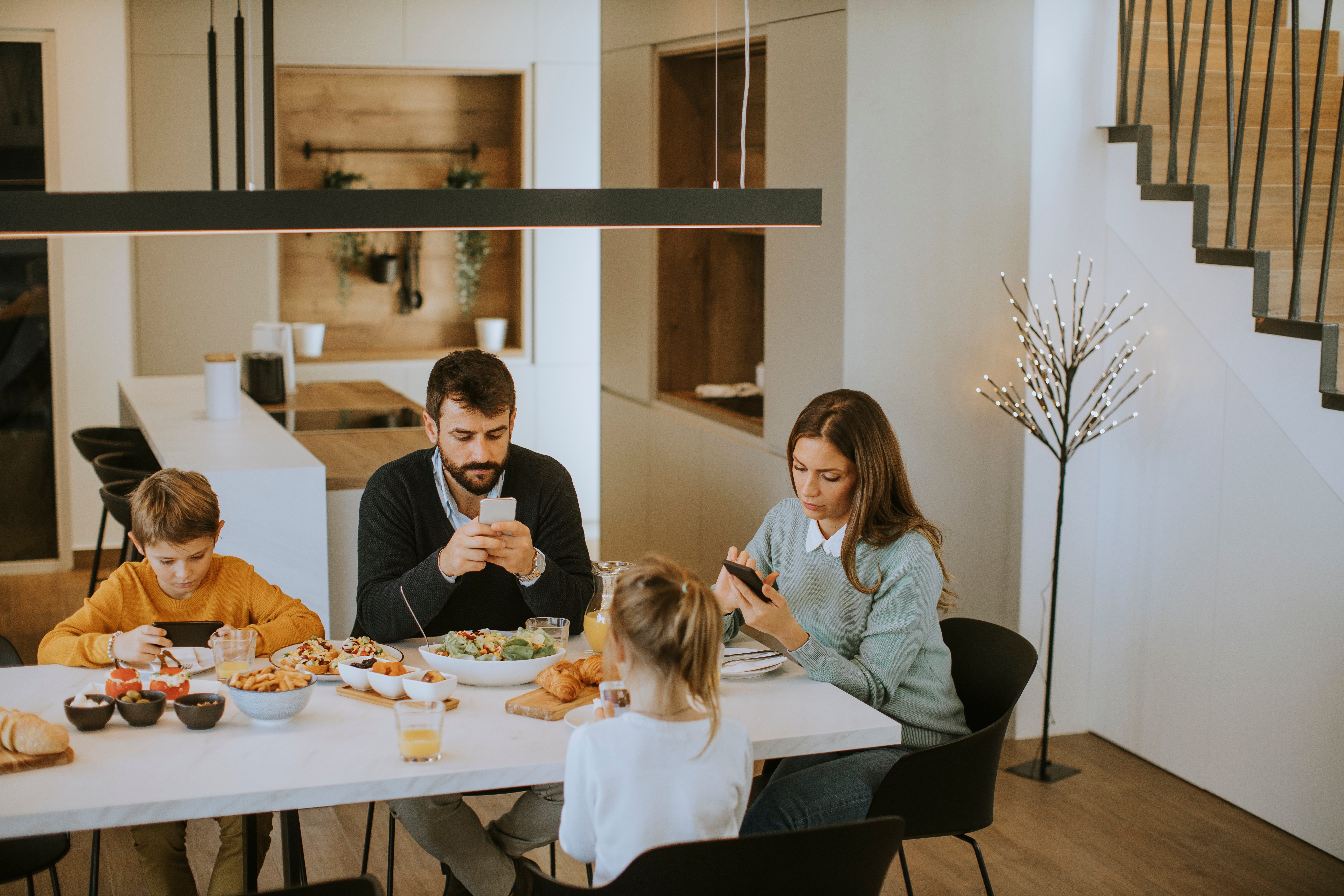 Erwachsene und Kinder sitzen beim Essen und sehen in ihre Smartphones