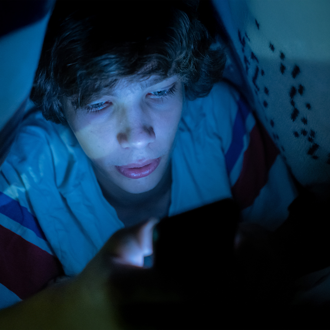 Ein Junge schaut unter der Bettdecke auf sein Handy. DGK_Artikel-02_What-is-Cybergrooming.jpg