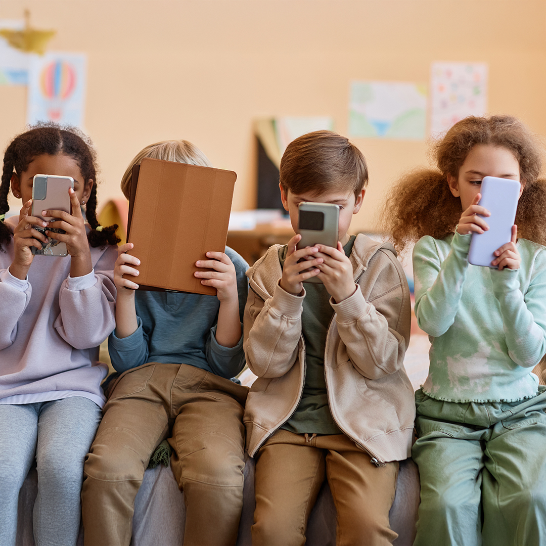 Vier Kinder sitzen nebeneinander und halten Smartphones oder ein Tablet vor das Gesicht. DGK_Artikel-18_Use-of-media.jpg