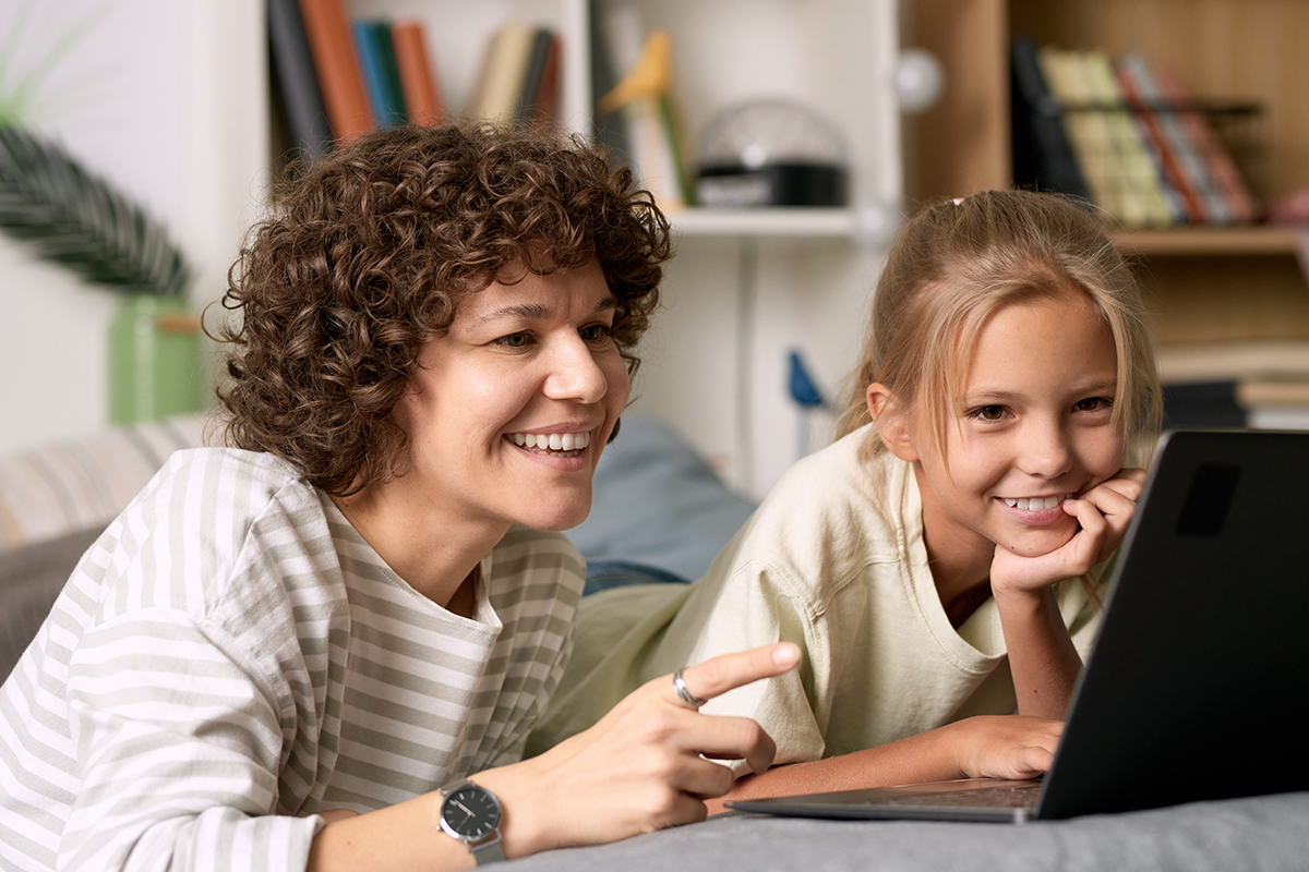 Zwei Kinder sitzen lächelnd vor einem Laptop und erkunden gemeinsam digitale Inhalte.