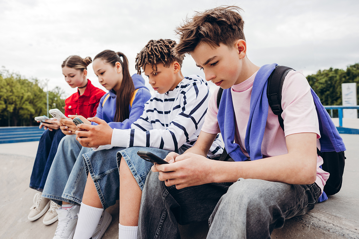 Jugendliche sitzen in der Reihe im Freien und schauen auf ihre Smartphonesn