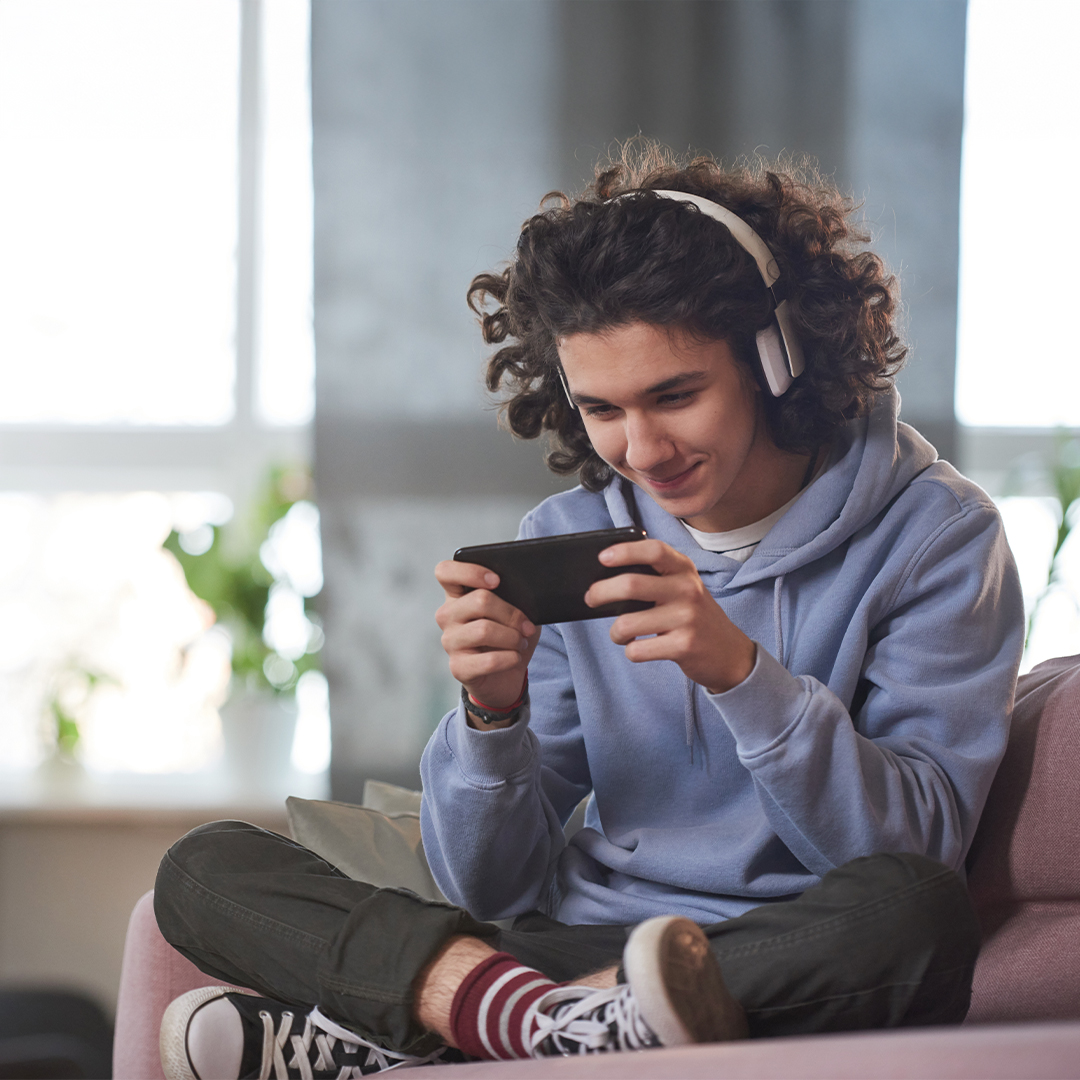 Junge mit Kopfhörern spielt im SChneidersitz auf seinem Smartphone 20260910_DGK_Q4_Artikel_NEW-Roblox.jpg