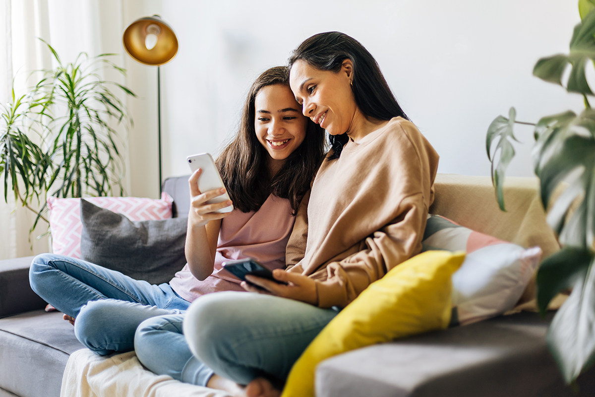 Mutter und Tochter sitzen auf dem Sofa. Die Tochter zeigt der Mutter etwas bei TikTok auf ihrem Smartphone