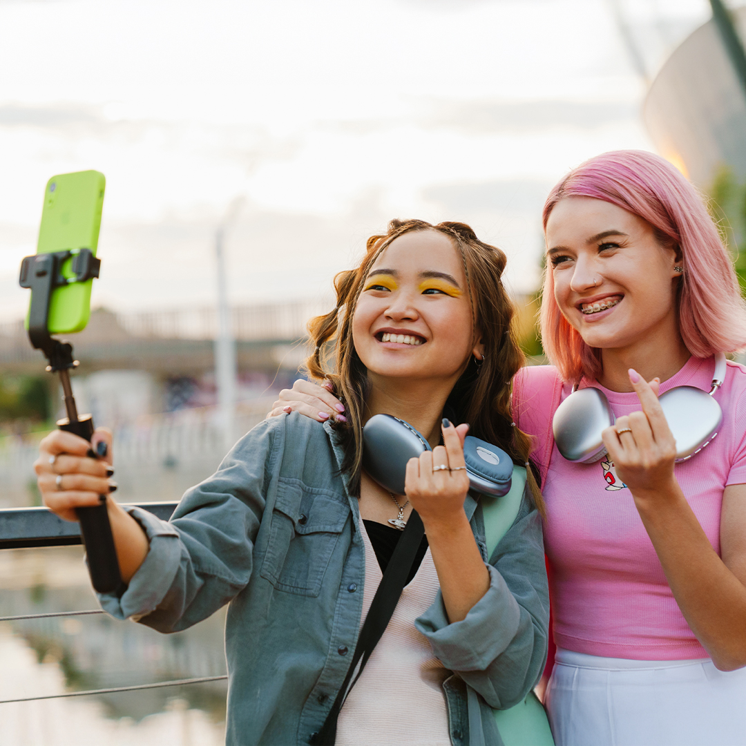 Zwei junge Frauen stehen nebeneinander, zeigen mit ihren Fingern ein Herz und posieren mit einem Smartphone auf einem Selfie-Stick. 20260910_DGK_Q4_Artikel_NEW-TikTok.jpg