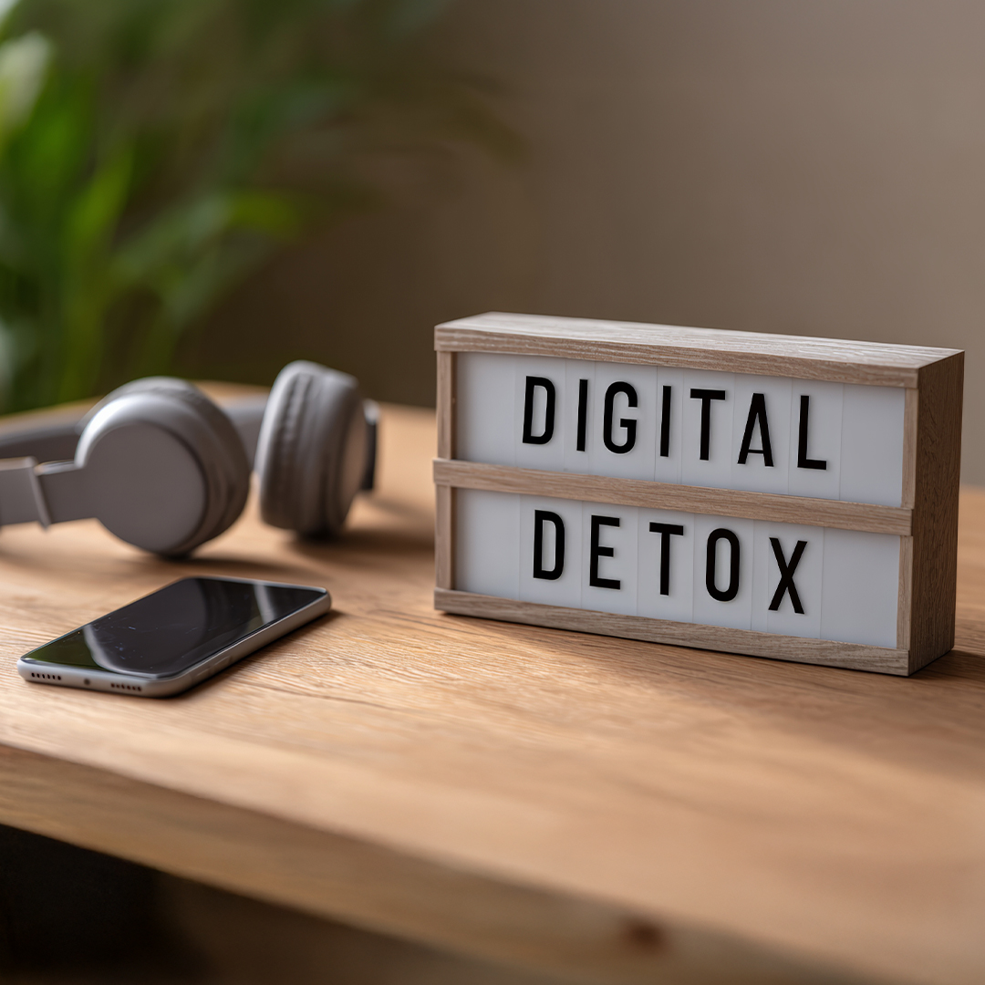 Leuchtbox mit Aufschrift „Digital Detox" auf Holzoberfläche, daneben abgelegtes Smartphone und Kopfhörer – Symbol für digitale Auszeit im Familienalltag 20251215_DGK_Eltern_Artikel_Digital-detox-in-everyday-family-life.jpg
