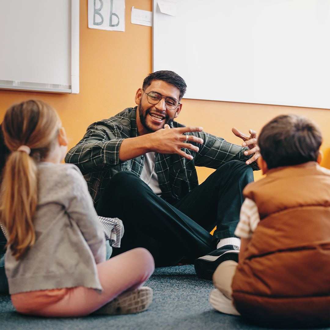Junger Mann sitzt mit zwei Kindern auf dem Boden und erklärt etwas gestenreich in einem hellen Raum DGK_Artikel-19_Use-of-media.jpg
