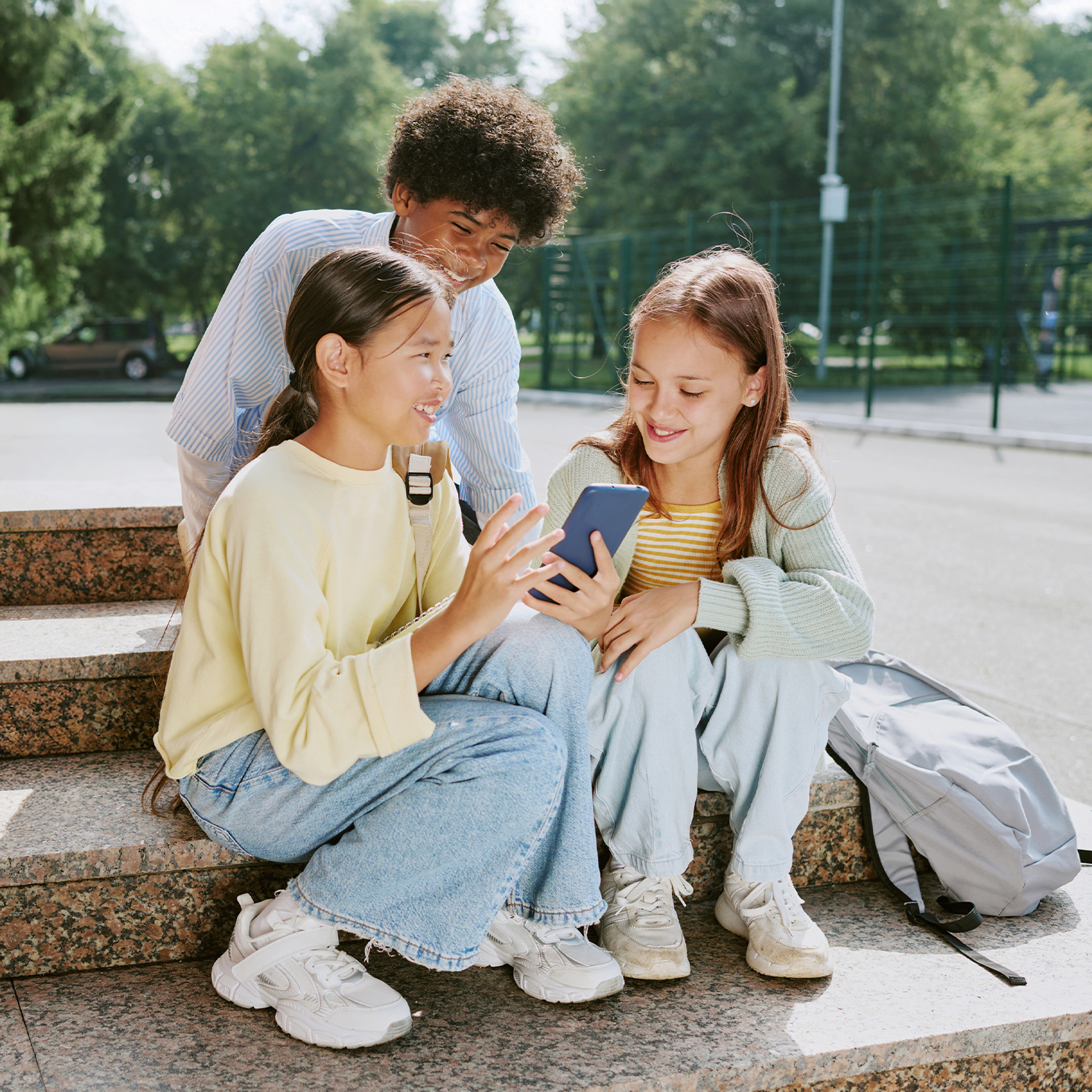 Drei Schüler:innen mit Schulrucksäcken nutzen gemeinsam Smartphone, positives Vorbild digitale Gesundheit
