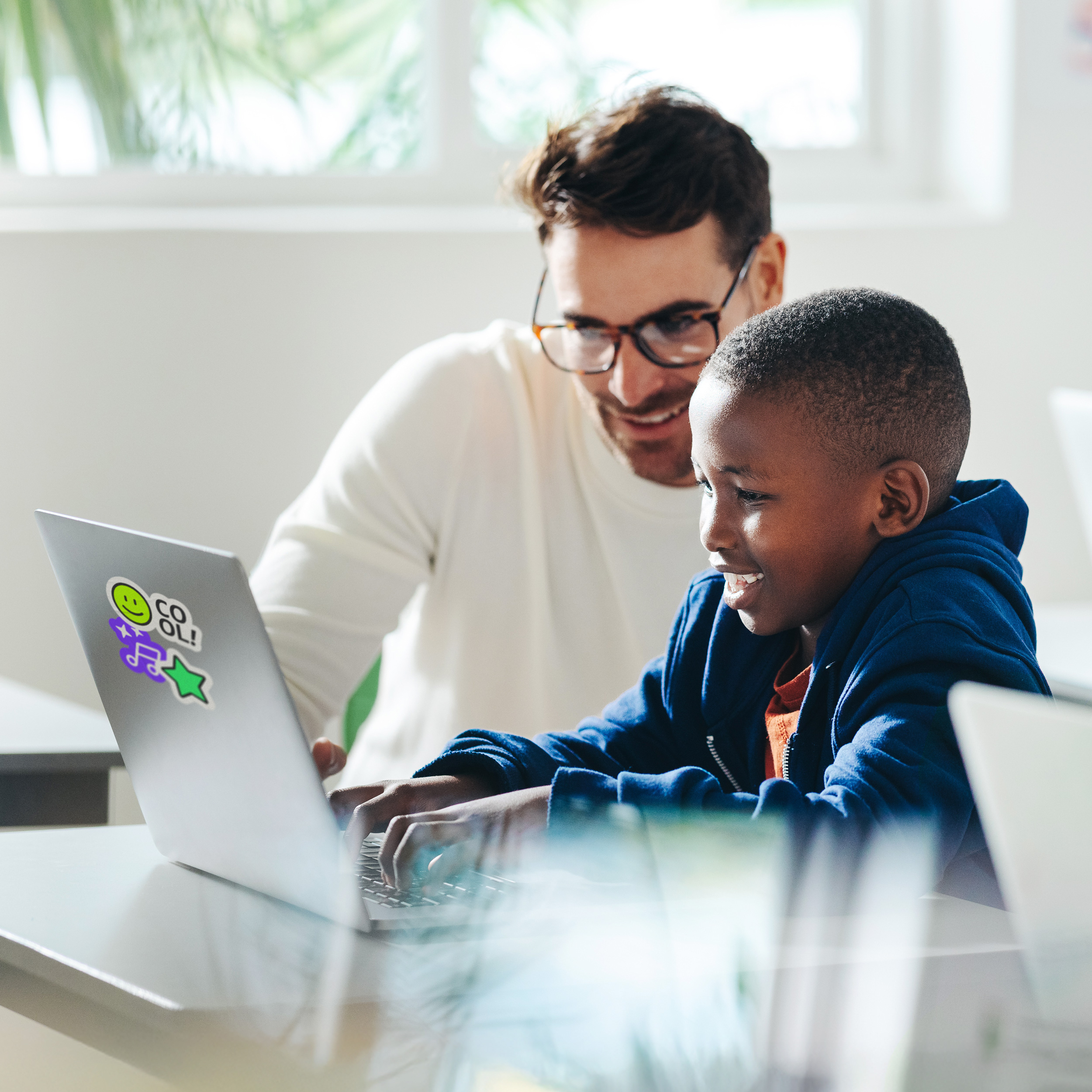  Vater unterstützt Sohn am Laptop beim Erlernen digitaler Kompetenzen